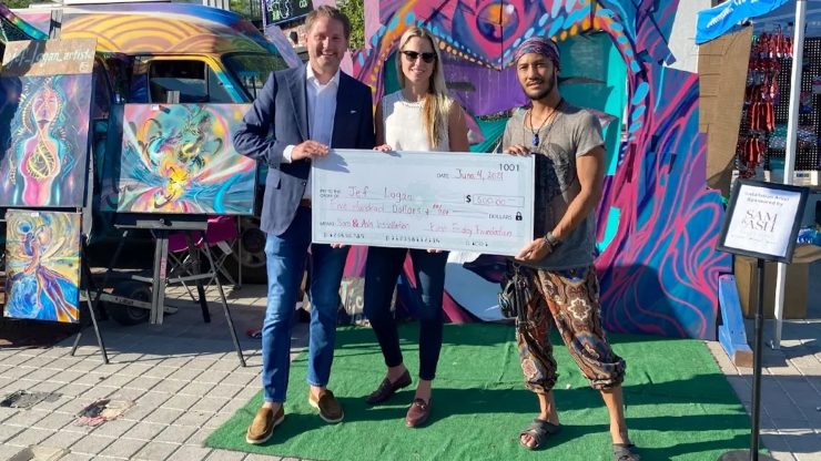 Three individuals proudly present a large check against a vibrant backdrop, symbolizing community support.