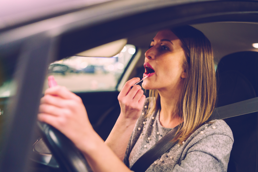 Young woman sitting in the car on the driver's seat putting lipstick while driving