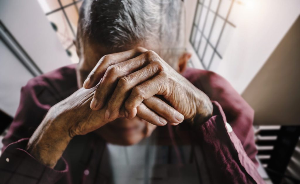 elderly person holding their hands in front of their face