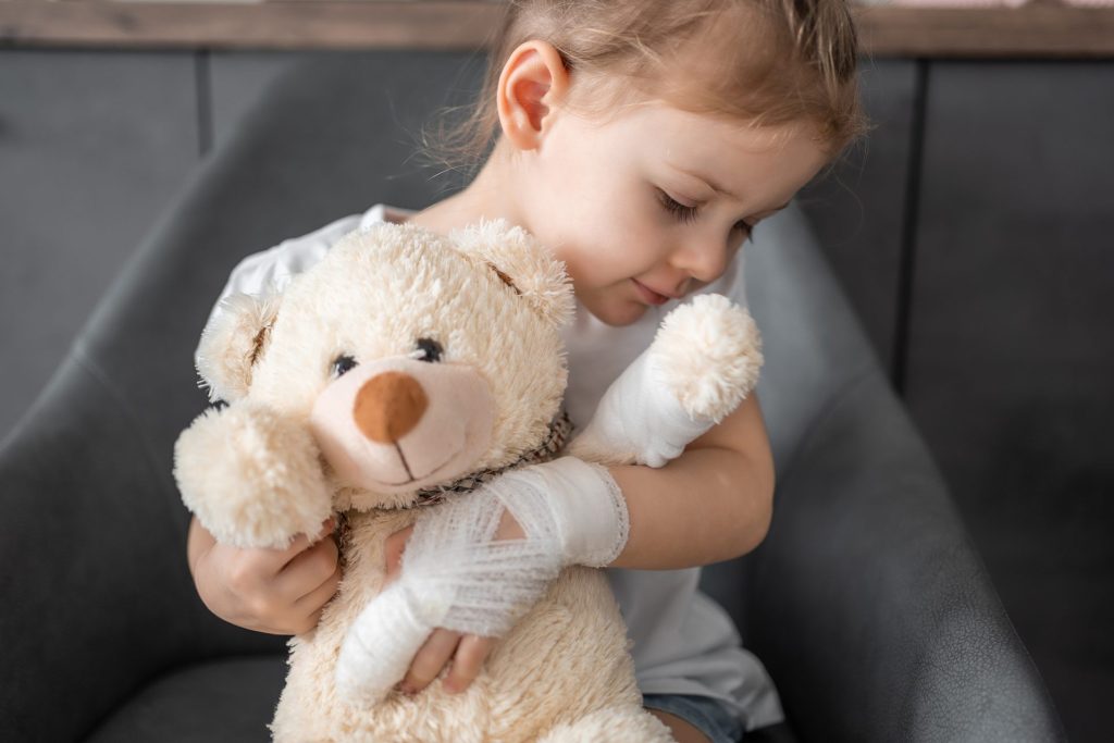 child with bandage on hand hugging a teddy bear
