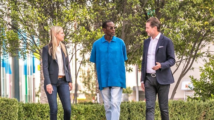 Three professionals engage in a thoughtful conversation amidst a vibrant, green setting.