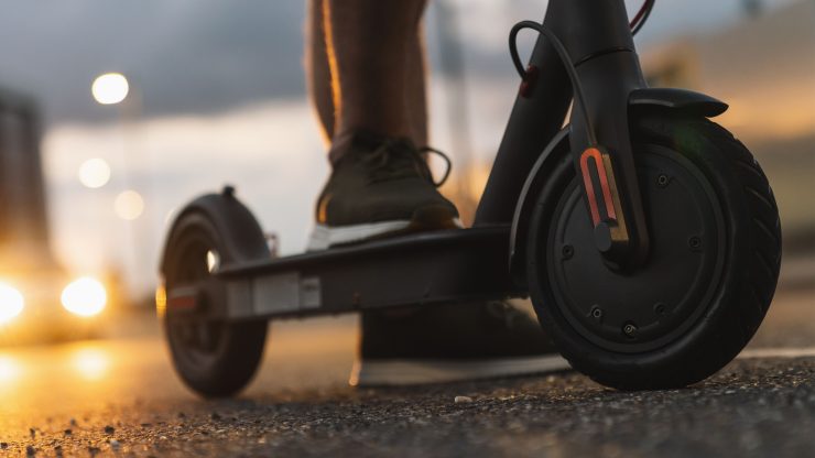 A person confidently rides a scooter on a dimly lit street, reflecting urban mobility and resilience.