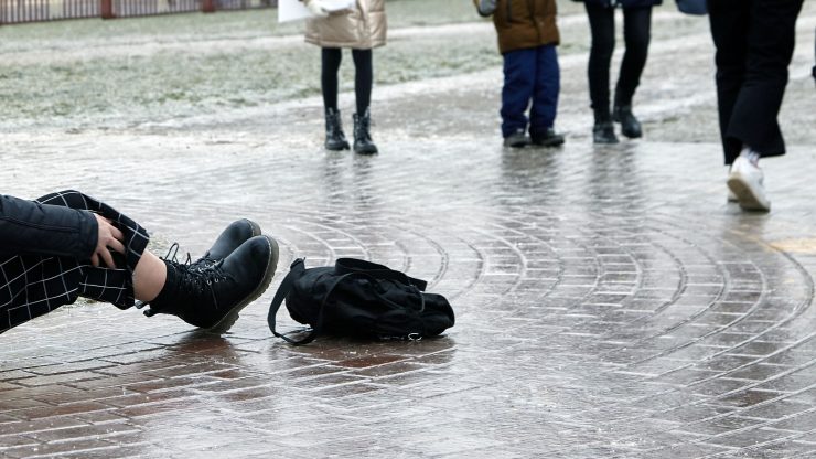 A person sits on the ground, appearing injured, as others walk by, highlighting community awareness.