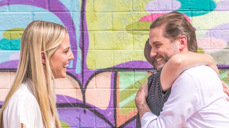 A warm exchange between three individuals against a vibrant mural, reflecting support and camaraderie.