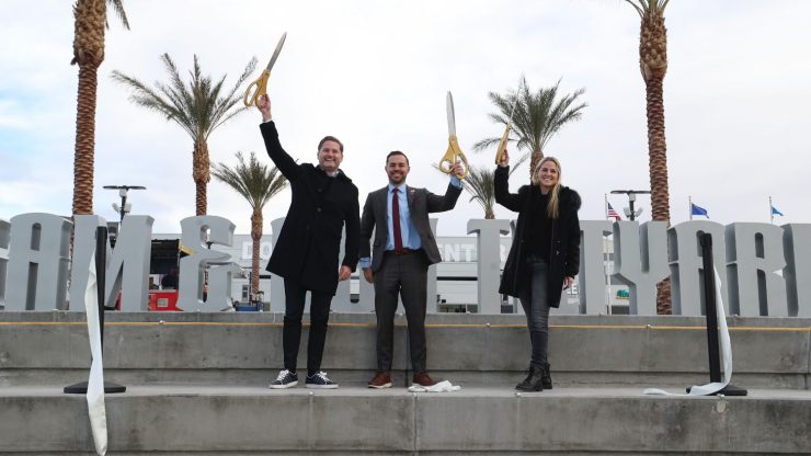 Three confident individuals celebrate a new beginning, holding oversized scissors amidst a lively setting.