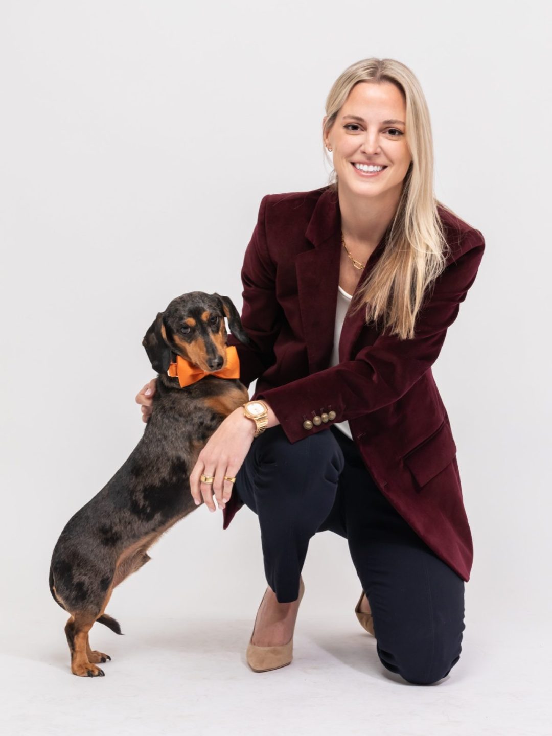 A confident attorney kneels beside a friendly dog, exuding warmth and approachability in a professional setting.