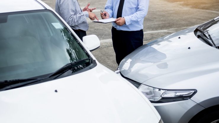 Two men discuss details after a car accident, showcasing collaboration and support in a challenging situation.