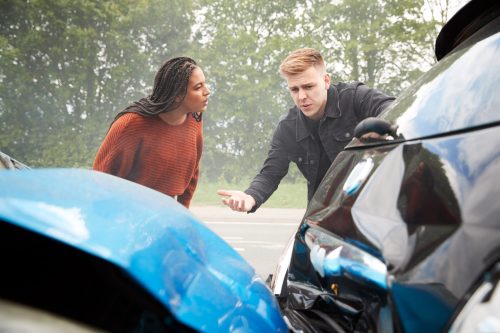 A serious discussion unfolds between two individuals by damaged cars, reflecting concern and accountability.