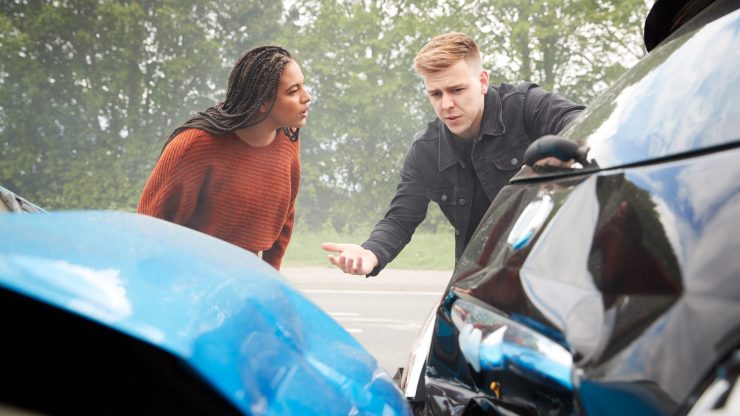 A serious discussion unfolds between two individuals by damaged cars, reflecting concern and accountability.