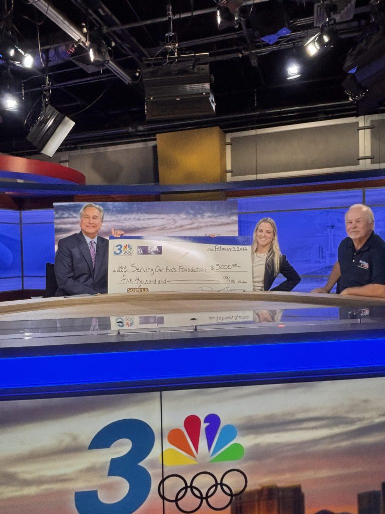 Three individuals proudly present a large check in a professional studio, embodying community support and advocacy.