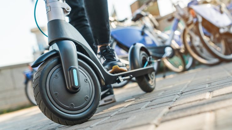 Close-up of a person standing on an electric scooter in an urban setting, emphasizing safety and mobility.