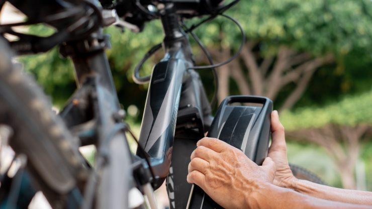 Senior cyclist securing an electric bike battery outdoors, emphasizing safety and care.