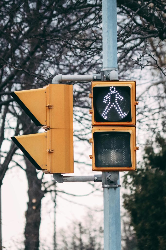 Pedestrian crossing signal glowing white amid bare trees, symbolizing safety and vigilance.