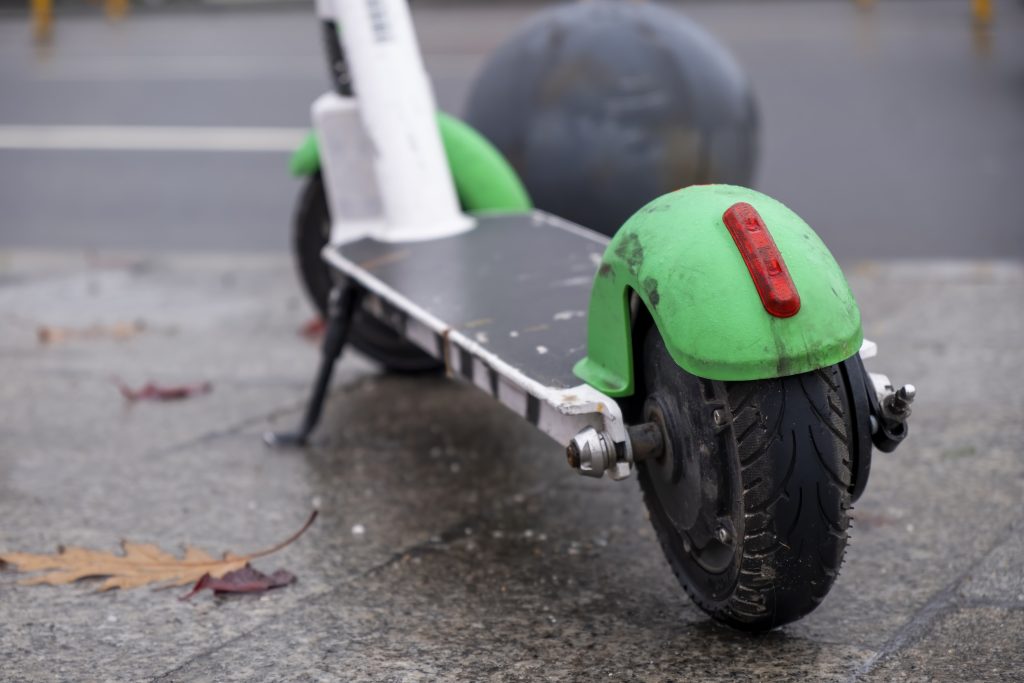 Parked green electric scooter on wet pavement, symbolizing urban mobility and safety awareness.