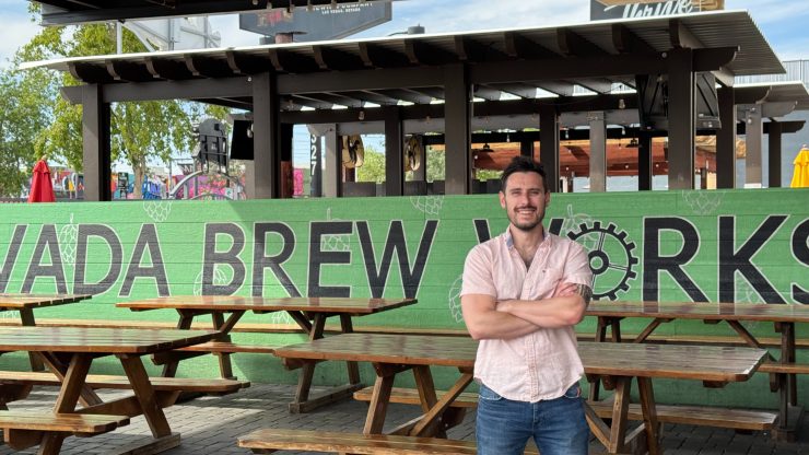 Confident man standing with arms crossed in relaxed outdoor seating area with green branded wall behind.