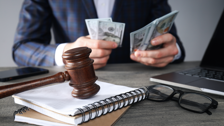 Gavel on desk with legal notebooks and confident professional counting settlement money.