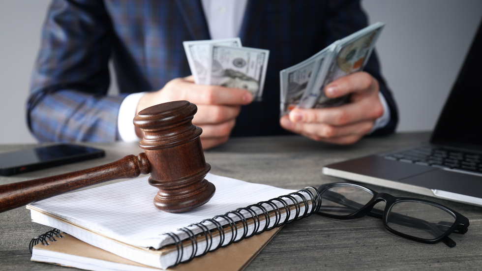 Gavel on desk with legal notebooks and confident professional counting settlement money.