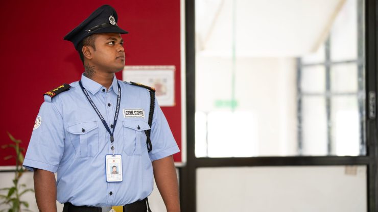 Security guard in uniform standing alert at a building entrance.