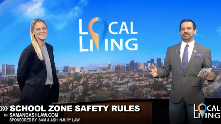 Two professional hosts discuss school zone safety on a local news set with city skyline backdrop.