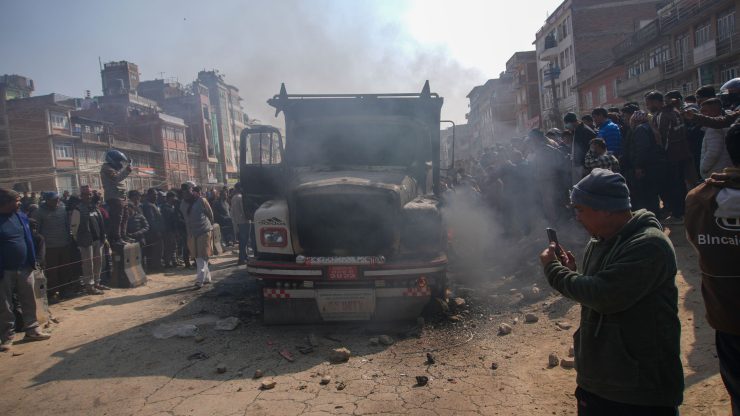 A crowd gathers around a smoky truck in a busy urban street, capturing the scene.