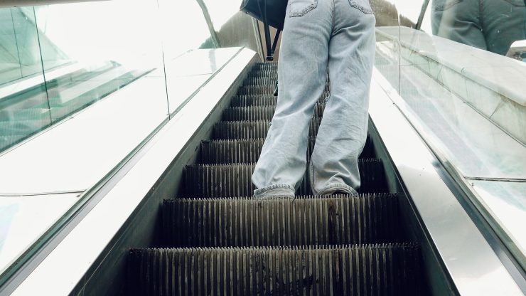 Casual woman with long hair on an outdoor escalator, city background.